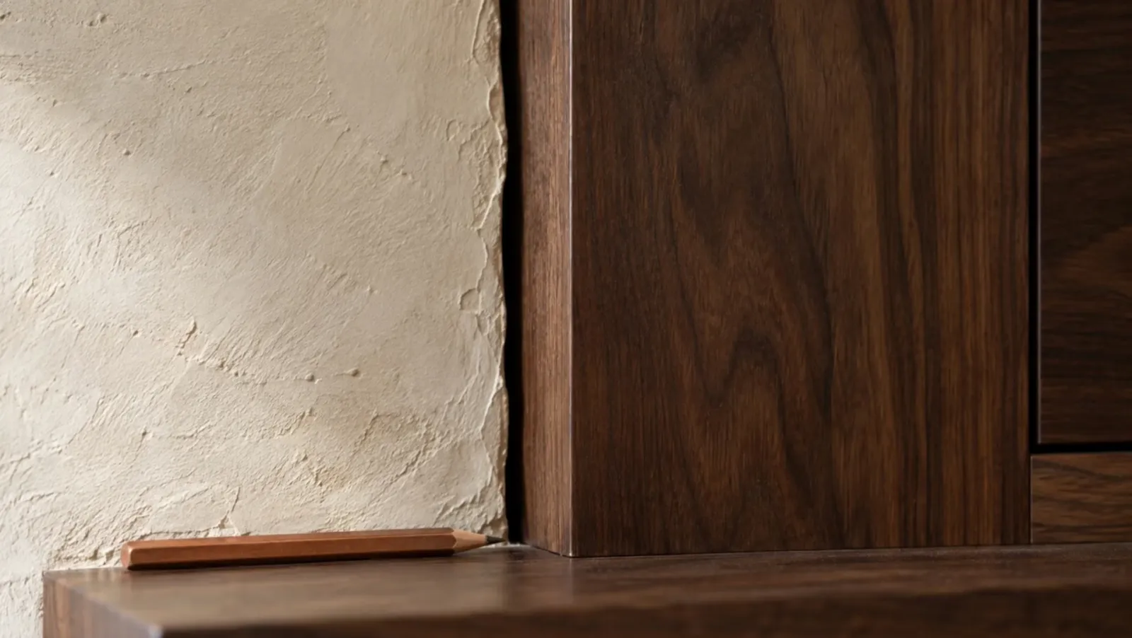 Illustrative detail of an uneven plaster wall beside a straight walnut cabinet panel